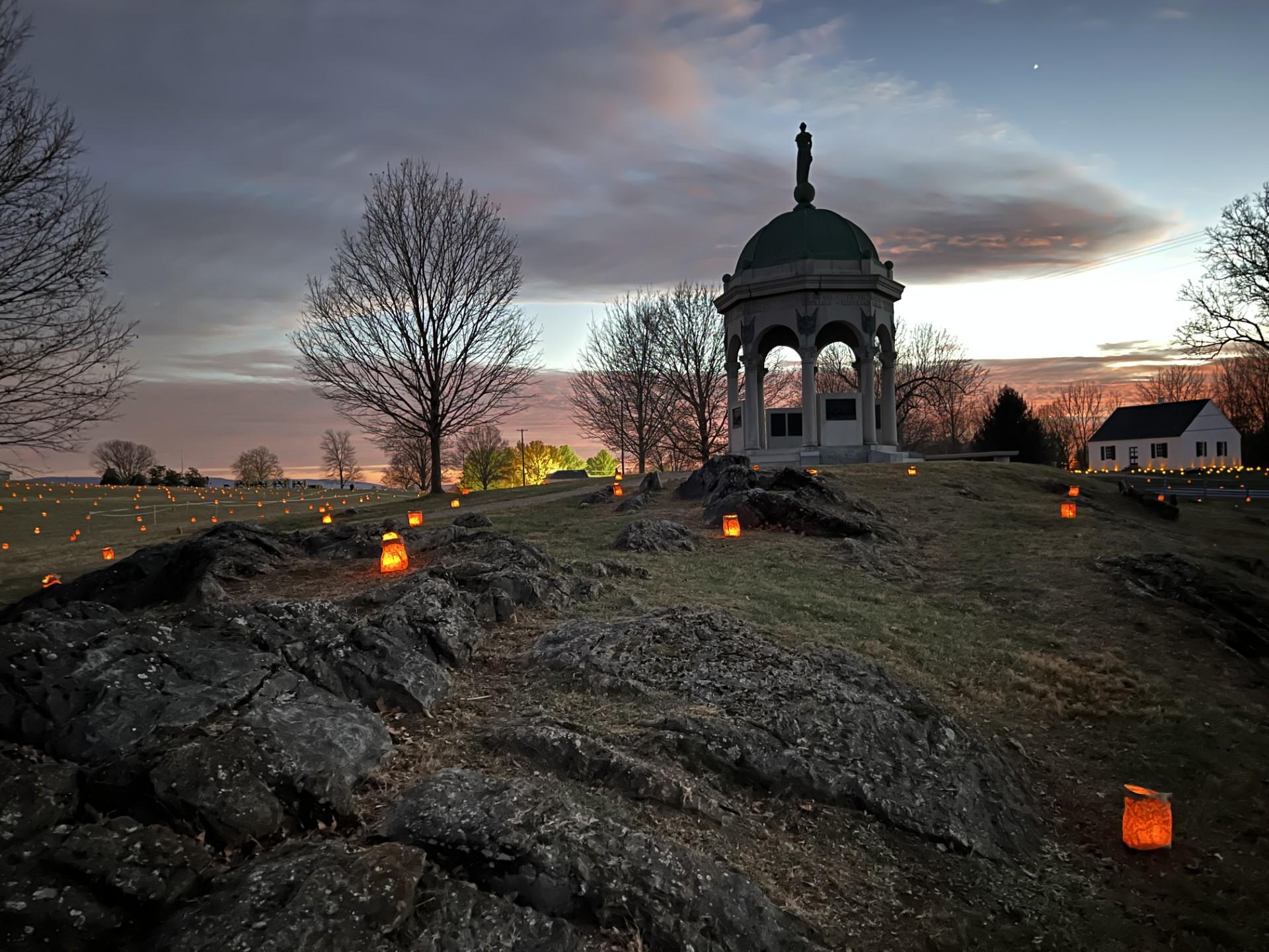luminaries placed by Maryland Monument with dramatic orange red clouds