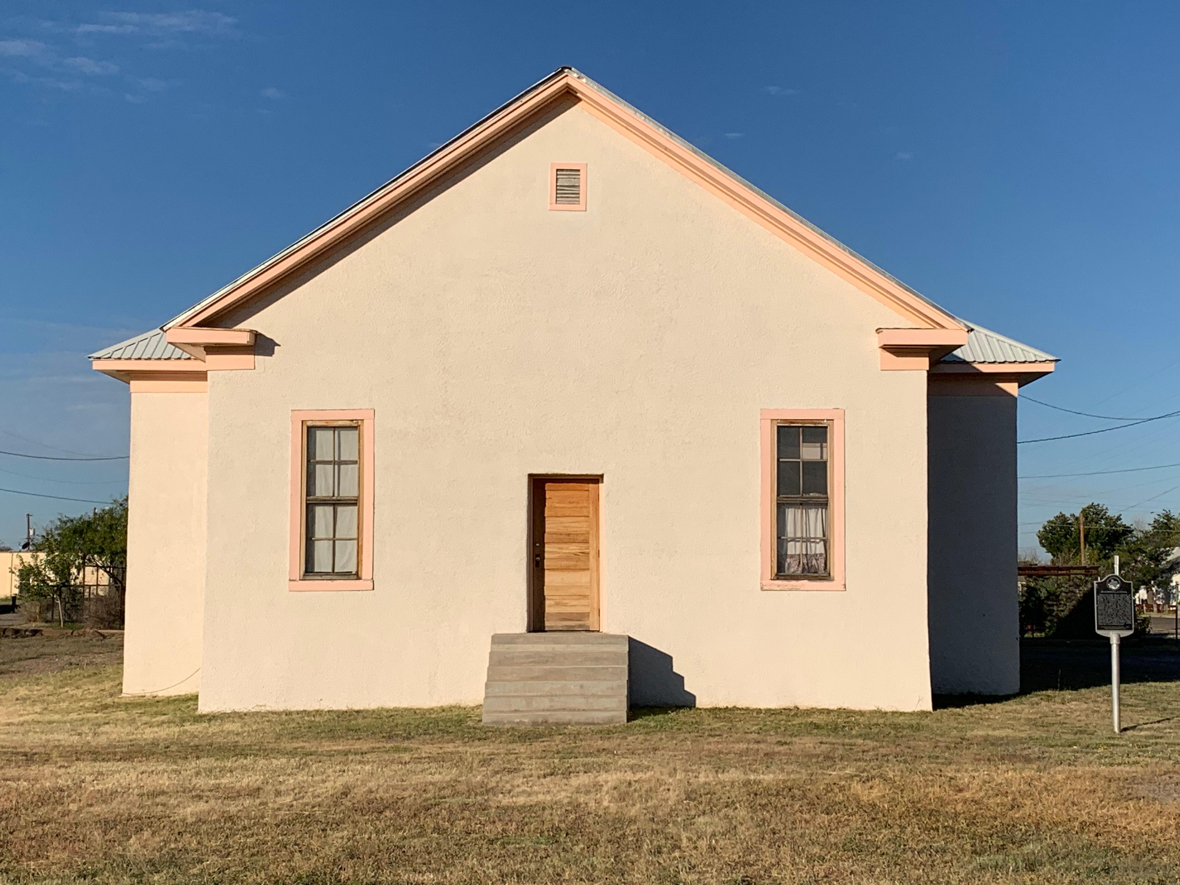 cream colored building with two windows and a wooden doorway with steps leading up to it.