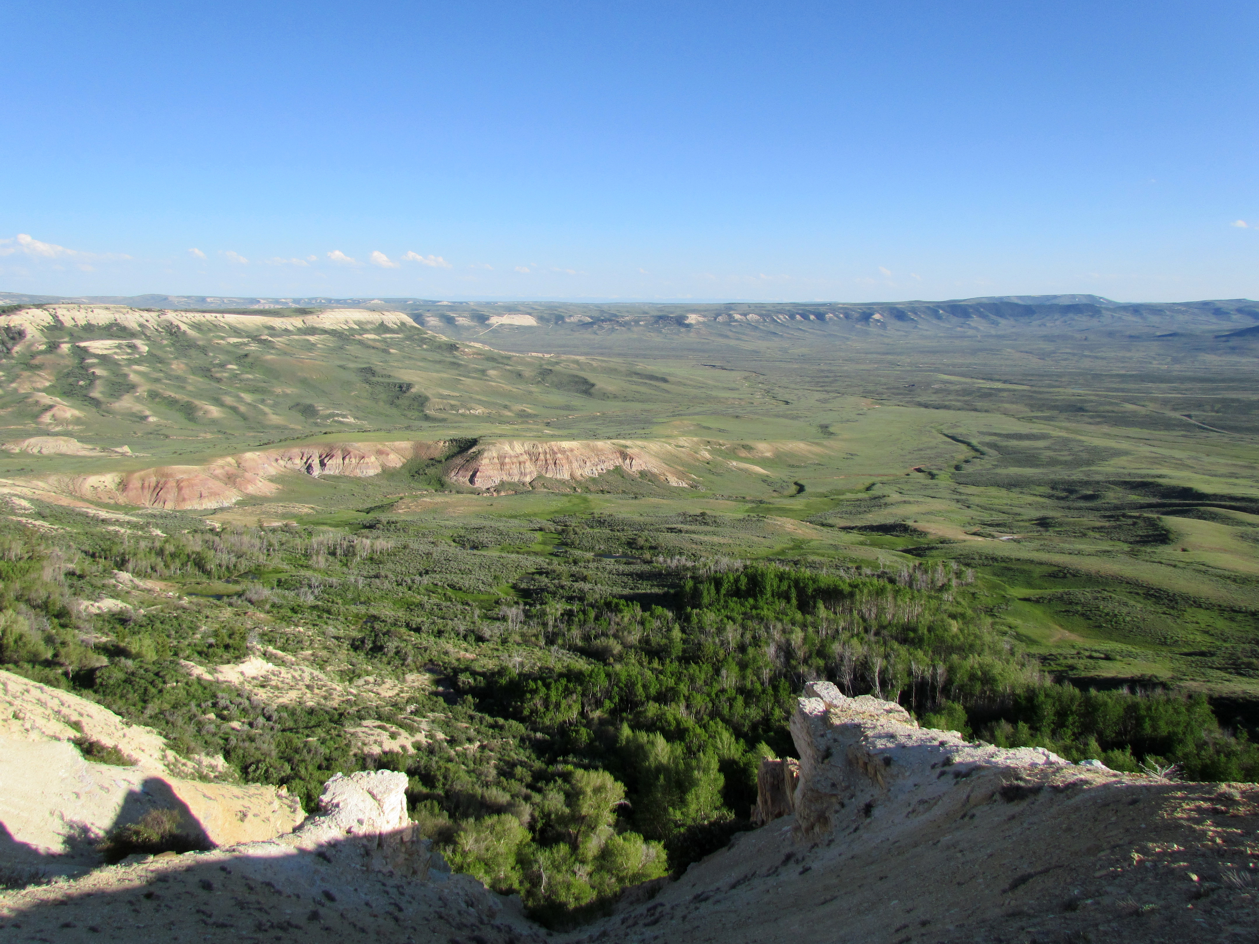 A green valley with distant tan and red ridges. The foreground is a cliff's edge.